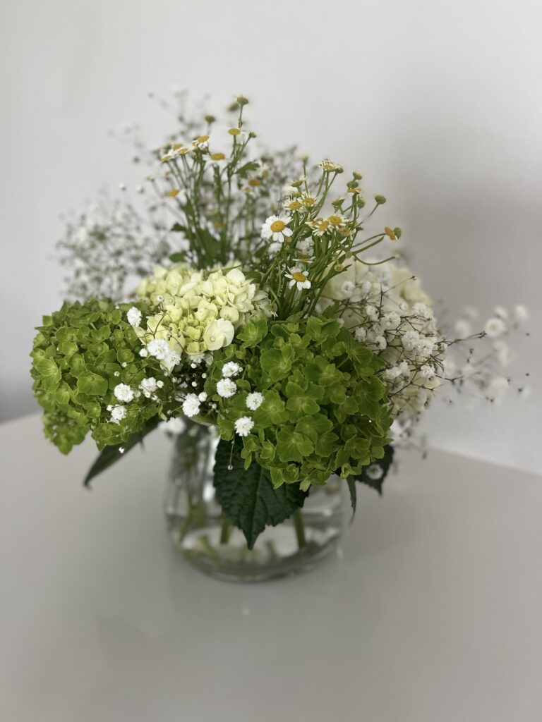 The final result: green and white hydrangeas, baby's breath, and chamomile arranged in a glass vase