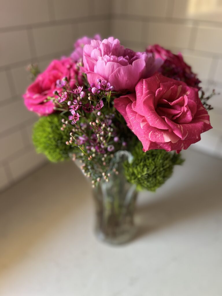 The final result: pink striped roses and peonies, green ball dianthus, and purple waxflower arranged in a glass vase